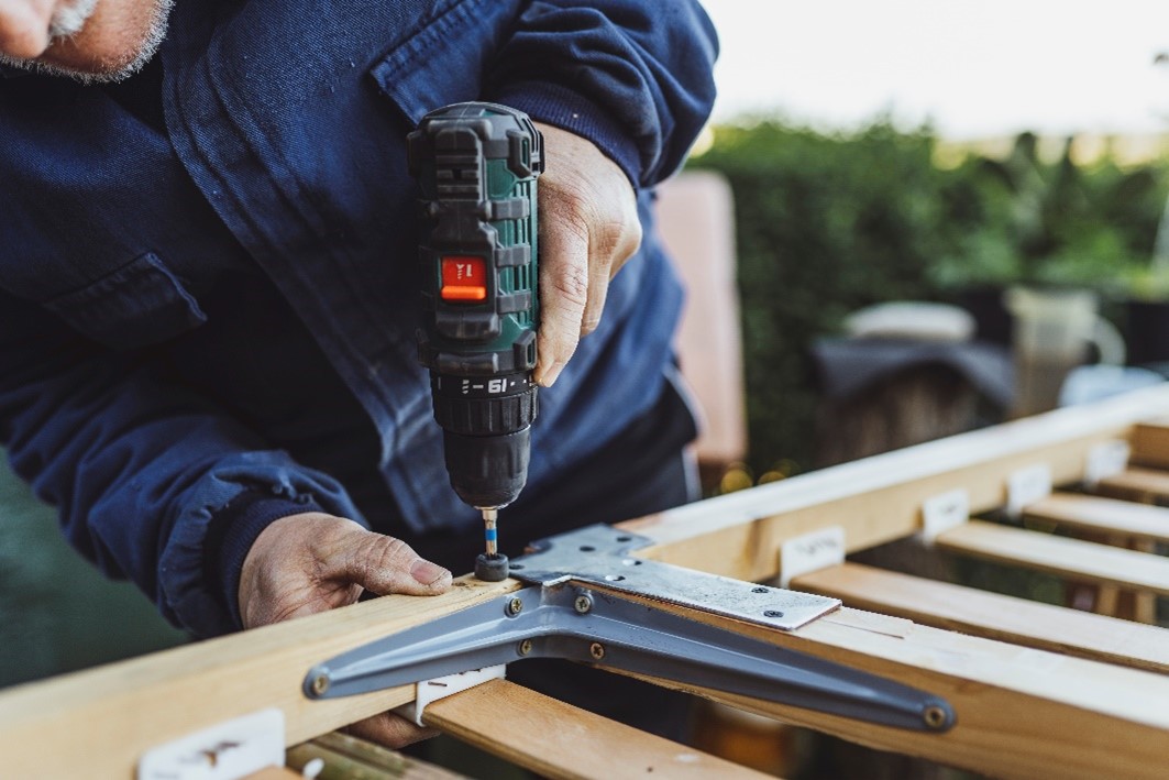 A man uses a drill to connect supportive beams of a house